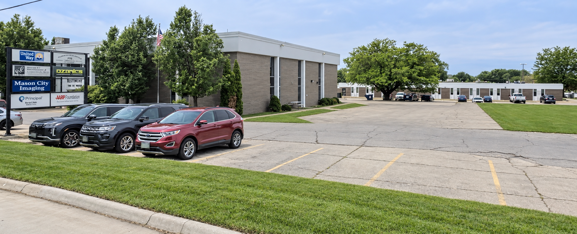 Street view looking west from S Pierce Avenue, with Iowa Specialty Clinic at Westbrook Office Park on the left and the subject property across the paved area on the right. Grounds digitally tidied for presentation review.